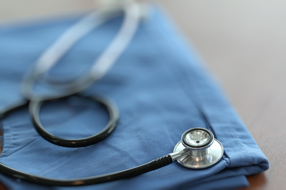 Stethoscope with blue doctor coat on wooden table with shallow DOF evenly matched and background